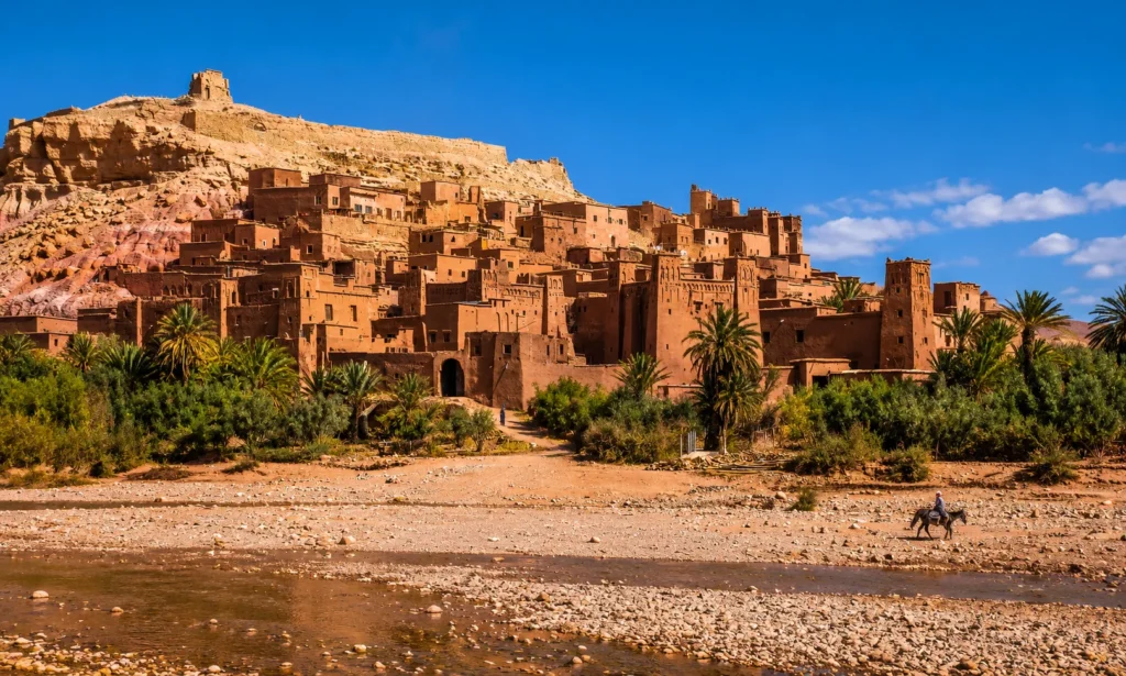 Ait Ben Haddou kasbah overlooking palm trees and a rocky riverbed in Morocco
